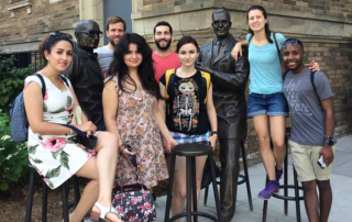 2018 Summer by Design participants pose with statues of Ernest McCulloch and James Till outside MaRS building in Toronto.